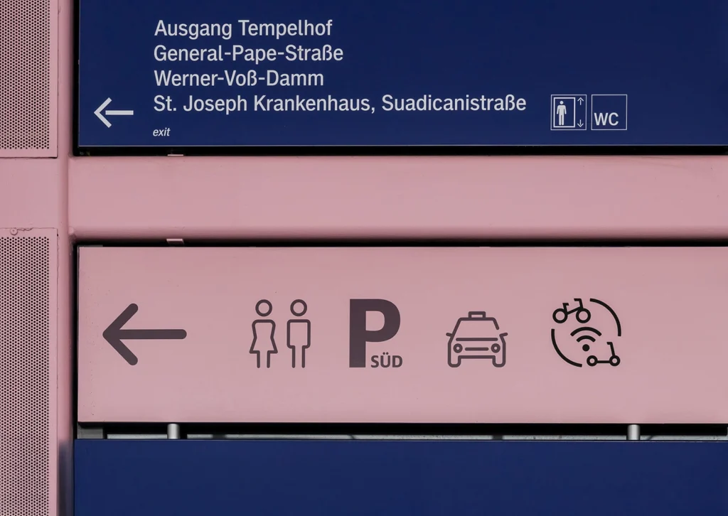 Bahnhofsbeschilderung mit Richtungspfeil und verschiedenen Piktogrammen, rechts ergänzt um das von R211 entwickelte Mobility-Hub-Icon für Fahrrad, E-Scooter und digitale Verbindung