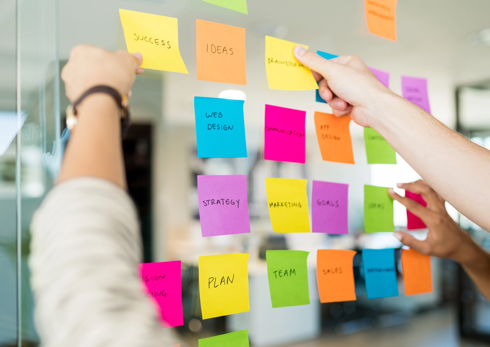 Aufnahme aus einem R211-Workshop zur Entwicklung einer User Journey: Zwei Personen kleben Post-its an eine Glaswand und sortieren thematisch relevante Inhalte.