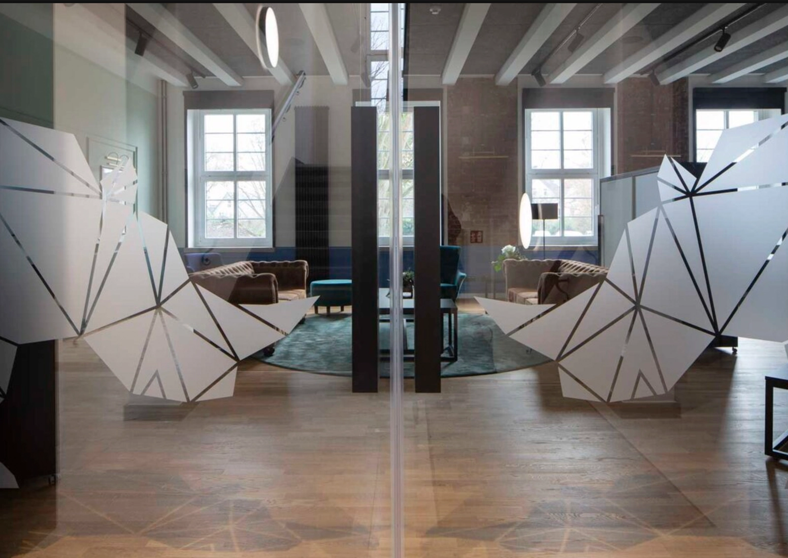 Aufnahme der räumlichen Markenanwendung für den SEH BildungsCampus Herford: Logo im Anschnitt auf Glastüren, im Hintergrund Blick in die Lounge.