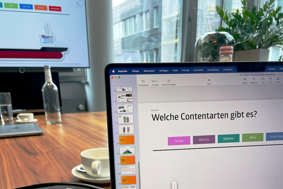 Aufnahme aus einem Social Media Workshop im Tagungsraum: Im Hintergrund ein Monitor mit angeschnittenen Inhalten zum Thema, im Vordergrund ein Konferenztisch. Durchführung und Konzeption durch die R211-Agentur.