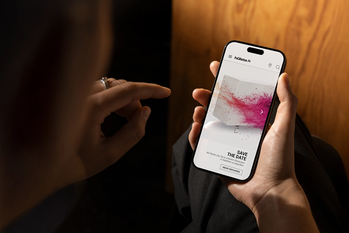 Nahaufnahme eines Smartphones, auf dem die hülsta Partnertage mit einem von R211 gestalteten Visual angezeigt werden. Eine Person hält das Handy in der Hand.
