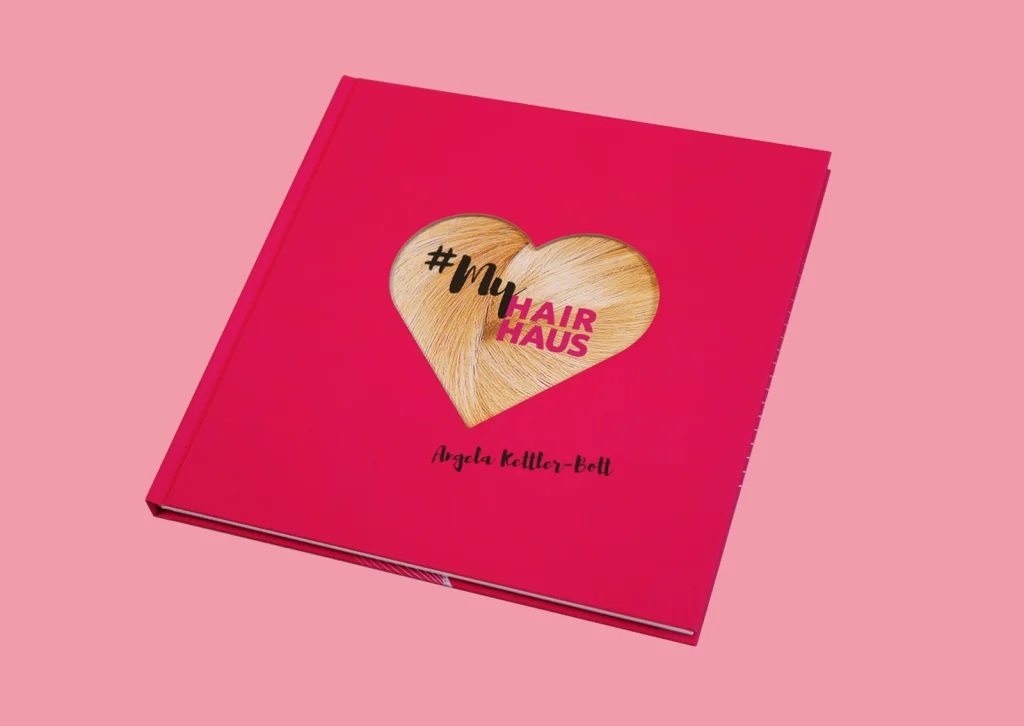 Pinkes Buch mit Herz-Motiv aus Haarsträhnen und der Aufschrift „#My Hair Haus“, darunter der Name Angela Keller-Bott