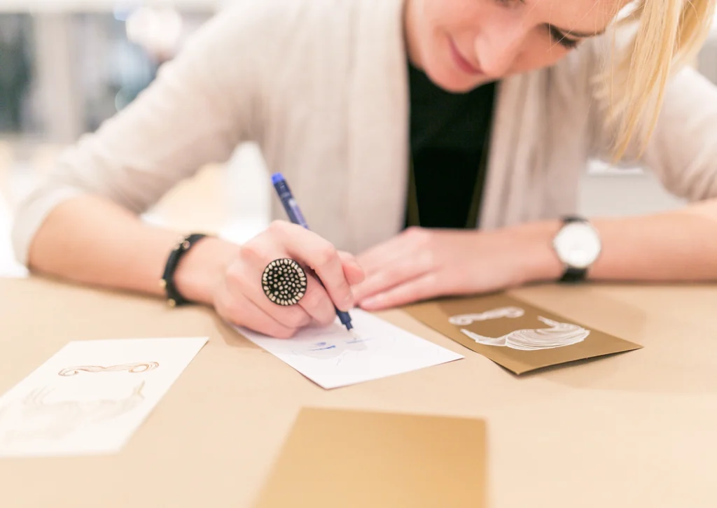 Nahaufnahme einer Eventbesucherin, die das präsentierte Papier testet und darauf schreibt. Aufnahme vom Paper Playground Event von Freytag & Petersen, visuell gestaltet von der R211-Agentur.