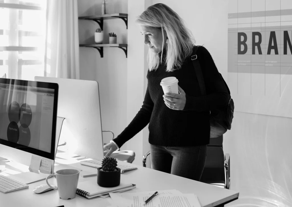 Eine Frau steht mit Kaffeebecher in einem Designbüro am Schreibtisch